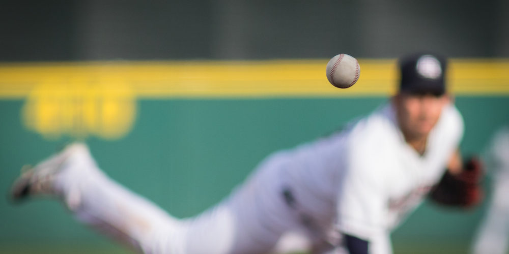 A,Baseball,In,Motion,With,Pitcher,In,Background.