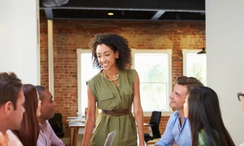 Manager femme debout en train de faire un tour de table avec son équipe de collaborateurs assis